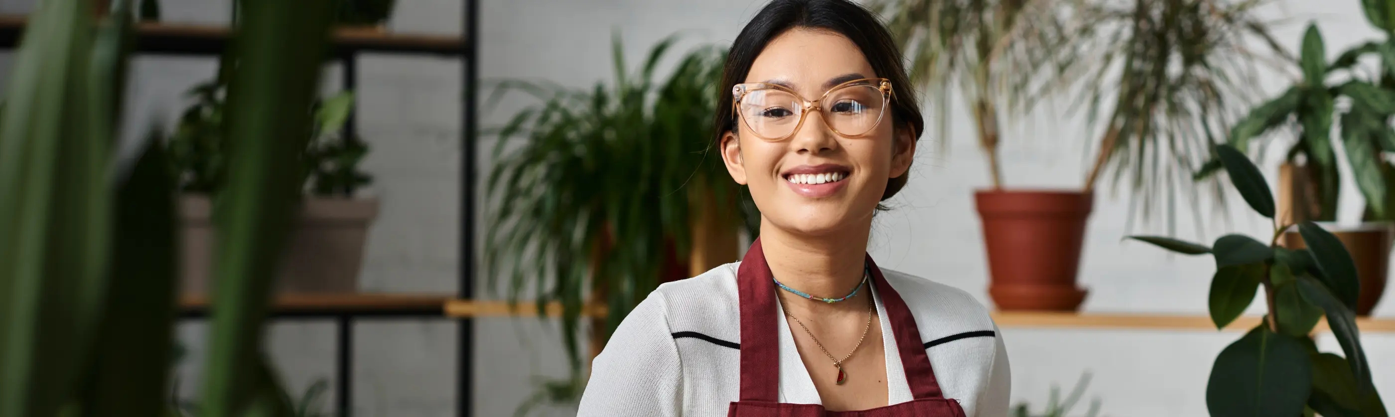 Mulher de óculos vestindo um avental no interior de uma loja de plantas e decorações.