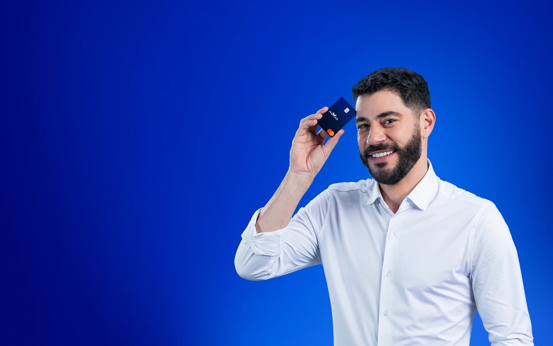 Evaristo Costa veste uma camisa social branca e está sorrindo para a câmera segurando um cartão Asaas ao lado do rosto.