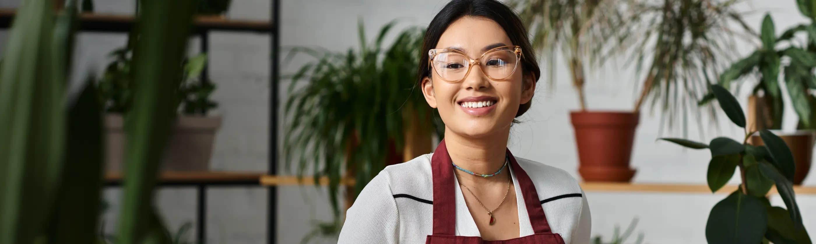 Mulher de óculos vestindo um avental no interior de uma loja de plantas e decorações.