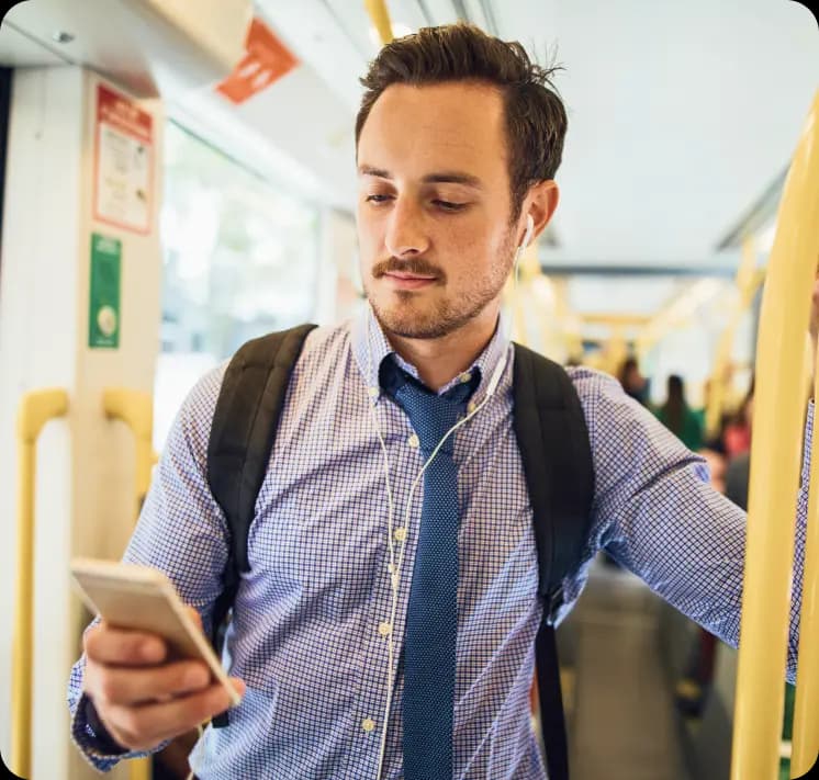 Empreendedor mexendo no celular enquanto está no transporte coletivo. Ele está usando uma camiseta social e gravata e leva consigo uma mochila.
