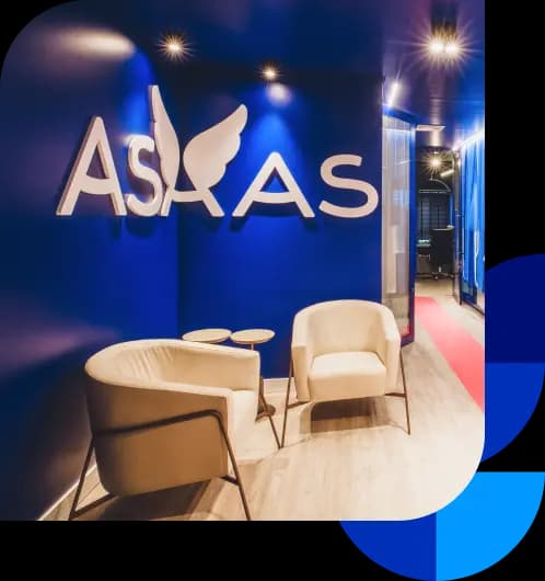 Hall de entrada do Asaas. Há duas poltronas bege e acima delas está o logo do Asaas. A parede é azul escuro e o chão é de piso laminado marrom claro. O lugar está bem iluminado.